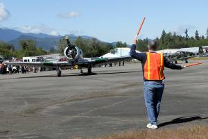 Tom Wayne Duke of Langley directs traffic as a North American SNJ-5 Texan based in Diamond Point taxies into a parking spot on Saturday at William R. Fairchild International Airport as part of Armed Forces & Public Safety Airport Appreciation Day and Fly-in. The event featured a variety of modern and vintage aircraft, flying demonstrations, public saftey displays and Young Eagles flights for children. (Keith Thorpe/Peninsula Daily News)