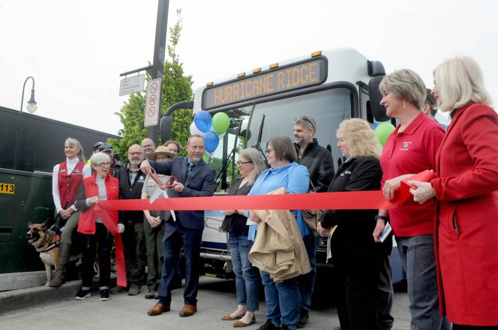 Clallam Transit General Manager Kevin Gallacci, with scissors, cuts a ribbon to inaugurate scheduled bus service from Port Angeles to Hurricane Ridge on Wednesday. (Keith Thorpe/Peninsula Daily News)