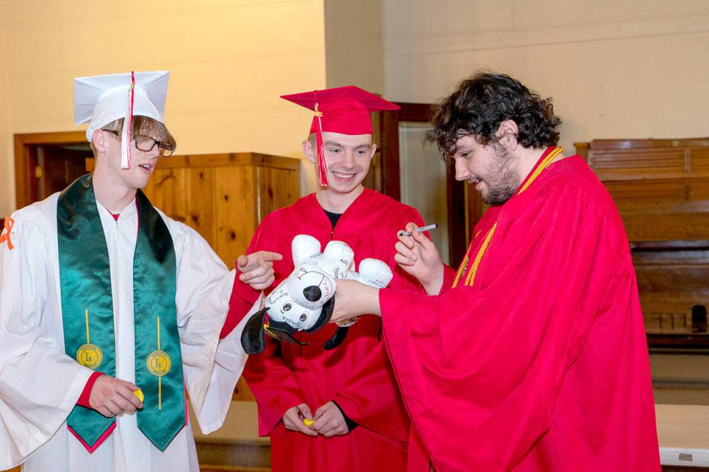 Port Townsend High Schools Duncan Kopala, right, signs the Signature Dog of Cameron Hemsiek, left, as Kenny Mustread, center, waits his turn. Eighty-two seniors received their diplomas before family and friends during the 132nd Commencement at McCurdy Pavilion on Friday night. (Steve Mullensky/for Peninsula Daily News)