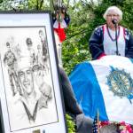 Joan Shields Bennett, wife of former Navy Seabee Marvin Shields, reads her remarks to assembled guests during a re-dedication of a plaque honoring her late husband, who died in Vietnam in 1965. Shields, portrayed in the drawing on the stand, was awarded the Congressional Medal of Honor for actions above and beyond the call of duty. The original plaque, made of bronze, was stolen in 2019 and was never recovered. (Steve Mullensky/for Peninsula Daily News)