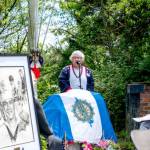 Joan Shields Bennett, wife of former Navy Seabee Marvin Shields, reads her remarks to assembled guests during a re-dedication of a plaque honoring her late husband, who died in Vietnam in 1965. Shields, portrayed in the drawing on the stand, was awarded the Congressional Medal of Honor for actions above and beyond the call of duty. The original plaque, made of bronze, was stolen in 2019 and was never recovered. (Steve Mullensky/for Peninsula Daily News)