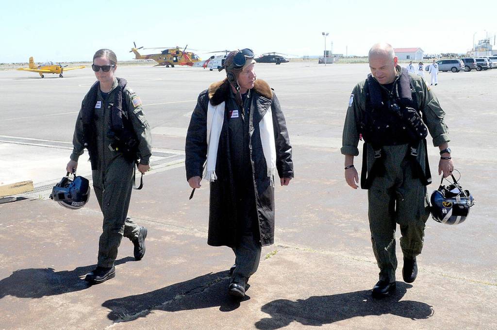 Cmdr. Joan Snaith, outgoing commanding officer of U.S. Coast Guard Air Station/Sector Field Office Port Angeles, left, and incoming officer Cmdr. Brent Schmadeke, right, enter the air station hangar with Rear Admiral Melvin Bouboulis, Commander of the Thirteenth Coast Guard District, after Thursdays unconventional change of command ceremony that took place during a helicopter flyby at the base. Bouboulis was dressed as the Ancient Albatross, honoring him as the active-duty Coast Guard member with the earliest graduation date from an aviation technical school. (Keith Thorpe/Peninsula Daily News)