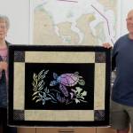 Mary Jeanne Richards and club Commodore Frank DeSalvo of the Sequim Bay Yacht Club display The Spirit of Honu, a quilt being raffled by the club to raise funds for Volunteer Hospice of Clallam County respite care services.
