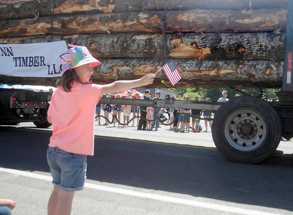 Ariel Gordob, 8, of Black Lake wakes a small flag as a log truck passes in the Joyce Daze Grand Parade on Saturday. (Keith Thorpe/Peninsula Daily News)