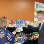 Derek Kilmer helps Port Angeles Food Bank Executive Director Emily Dexter fill up the shelves with some crackers inside The Market. (Dave Logan/for Peninsula Daily News)