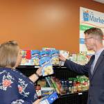 Derek Kilmer helps Port Angeles Food Bank Executive Director Emily Dexter fill up the shelves with some crackers inside The Market. (Dave Logan/for Peninsula Daily News)