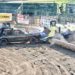 Demolition derby driver Morgan Seamonds (107) pushes Brandon Vales car (76) up and over a log barrier in a cloud of dust and exhaust in front of a sold-out crowd at the Clallam County Fairgrounds on Sunday evening. (Dave Logan/for Peninsula Daily News)
