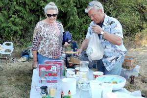 KEITH THORPE/PENINSULA DAILY NEWS
Marlene McCurdy of Port Angeles, left, purchases coffee mugs from Gary Gort of Port Angeles at a sale table in front of the Crescent Grange Hall in Joyce on Saturday. The location was one of dozens of garage and yard sales taking part in the Great Strait Sale, stretching along and near State Highway 112 from Port Angeles to Neah Bay.