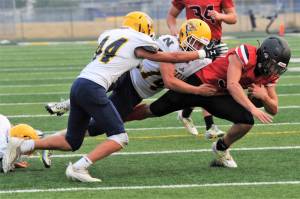 Neah Bay quarterback Julian Carrick is brought down by Naselle's Jack Strange (44) and Kolten Linstrom (14) on Saturday in Forks. Neah Bay shocked the powerhouse Comets 58-20. Lonnie Archibald/for Peninsula Daily News