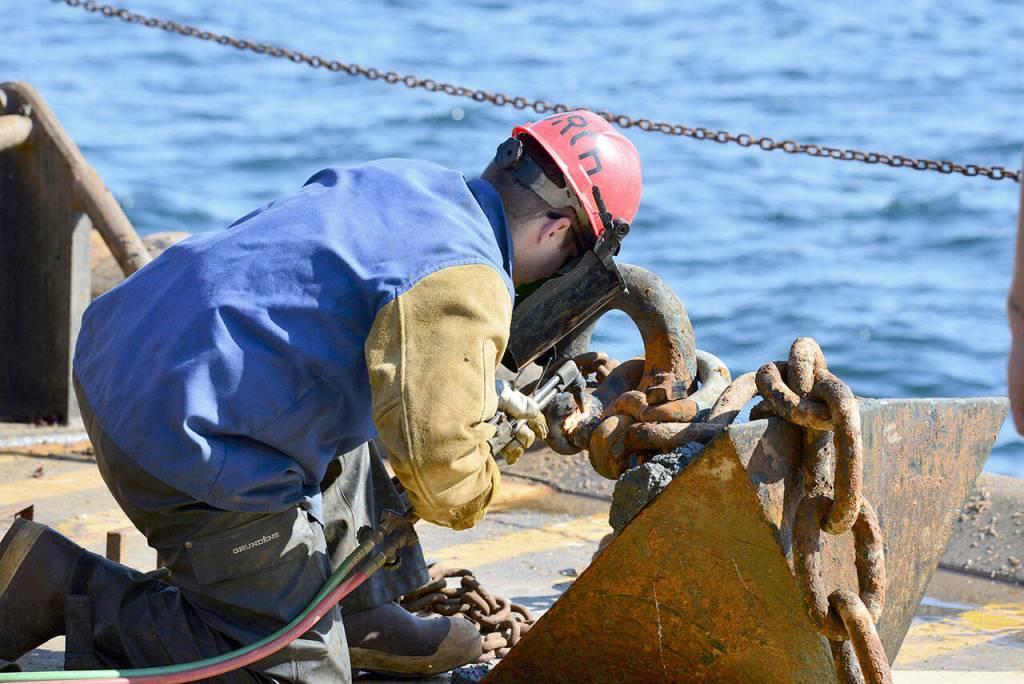 A crew member of the U.S. Coast Guard cutter Henry Blake cuts the chain off of an anchor used to hold a National Oceanic and Atmospheric Administration weather buoy in place in the Strait of Juan de Fuca on Tuesday, Sept. 20. Crews replaced several parts of the buoy, including the chain and rope used to keep it in place. (Peter Segall / Peninsula Daily News)
