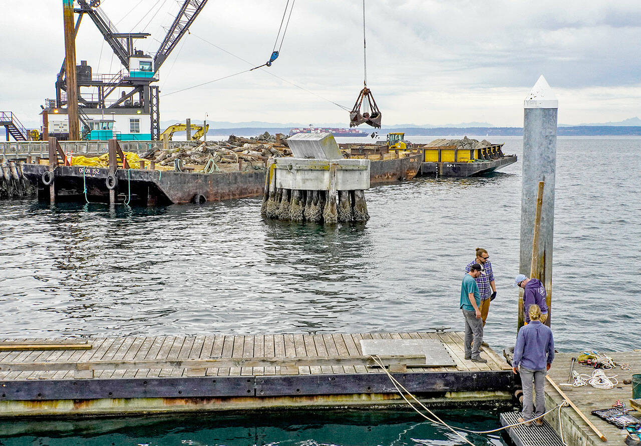 A crew from the Northwest Maritime Center facilities department, Sam Trocano, Jeff Hogue, Shane Meyer and Mike Conklin, work on the removal of the floating dock on the centers pier in preparation of winter winds and weather. In the background, work continues on the deconstruction of the entrance to the Point Hudson Marina by Orion of Tacoma. (Steve Mullensky/for Peninsula Daily News)
