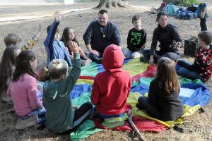Seaview Academy instructor Eric Pickens, top, and Olympic Nature Experience teacher Amanda Erickson, right, sit with Outdoor, Real-world, Child-centered Academic Program students during an outdoor gathering at Lincoln Park in Port Angeles. (Keith Thope/Peninsula Daily News)