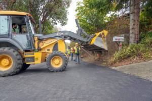 A road crew from the Port Townsend Public Works Department  Rafe Thornton, bucket driver, Tracy Benson, with hard hat, Chris MacDonald and Lane Dotson in the background  finishes repaving a section of Walnut Street on Thursday. The section of street was degraded for months with barriers set up to direct traffic around the worst part, essentially making it a one-lane roadway. The street was slated to be open for traffic later in the afternoon. (Steve Mullensky/for Peninsula Daily News)