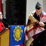 Kathryn Bates of North Olympic Peninsula Quilts of Valor, at the podium, helps present a quilt to U.S. Marine Corps veteran Wyatt Ranson on Friday. Ranson was one of 11 local veterans who received the honor on Friday at the American Legion Hall in Port Townsend. The Quilts of Valor volunteers make and present quilts to veterans of all branches of service in both Clallam and Jefferson counties. To request a quilt for a veteran, visit www.qovf.org or email 1katheybates@gmail.com. (Diane Urbani de la Paz/for Peninsula Daily News)