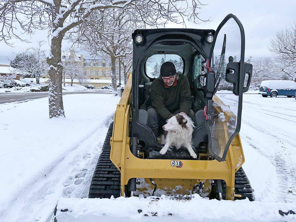 Jess Norton, with Wildflower Landscaping, sits in the cab of his Bobcat at the parking lot of the Port Townsend QFC with his Australian Shepherd Lucy while waiting for a call for his next destination for snow removal. Norton had just gotten back from clearing the Chase Bank downtown. (Steve Mullensky/for Peninsula Daily News)