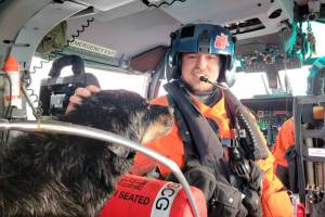 Petty Officer 3rd Class Austen Marshall, an avionics electrical technician and a flight mechanic at Coast Guard Air Station Port Angeles, sits near a dog his aircrew rescued from a grounded sailing vessel near Vancouver Island, British Columbia. The aircrew rescued one person and two dogs from the vessel. (U.S. Coast Guard courtesy photo)