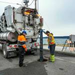 Rafe Thornton, left, and Lane Dotson, both with the City of Port Townsend Street, Sewer and Storm department, vacuum sewage out of the manhole and into the truck on Thursday, in order to facilitate repairs to the broken sewer line at Gaines and Water streets in Port Townsend on a newly installed sewer line damaged by recent storm and tidal activity. (Steve Mullensky/for Peninsula Daily News)