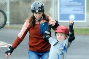 Shawna Bebo of Sequim lends a balancing hand to her son, Enzo Bebo, 7, at the Port Angeles Pump Track at Erickson Playfield in Port Angeles last weekend. The pair were on a family outing with a stop at the popular attraction. The 14,442-square-foot pump track is the largest Velosolutions pump track in the Pacific Northwest and the first public adaptive track in the nation. (Keith Thorpe/Peninsula Daily News)
