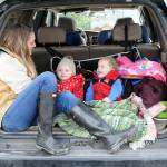 Katie Roszatycki of Port Angeles and her children, June Roszatycki, 2, and Asher Roszatycki, 3, sit in the back of their car waiting for the delivery of dry shoes and socks from another family member after an outing to Hollywood Beach on Thursday. The family was keeping themselves entertained in the parking lot at Port Angeles City Pier. (Keith Thorpe/Peninsula Daily News)