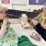 Loran Scruggs, left, brought a green cashmere sweater, a pair of floral silk pants and a pair of black cotton pants that needed to be mended to the Port Townsend Marine Science Centers Repair Cafe. Paula Lalish was one of three volunteers on hand to assist people by fixing clothing that had holes, rips, tears and and broken zippers. (Paula Hunt/Peninsula Daily News)