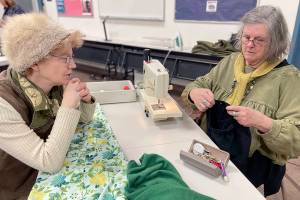 Loran Scruggs, left, brought a green cashmere sweater, a pair of floral silk pants and a pair of black cotton pants that needed to be mended to the Port Townsend Marine Science Centers Repair Cafe. Paula Lalish was one of three volunteers on hand to assist people by fixing clothing that had holes, rips, tears and and broken zippers. (Paula Hunt/Peninsula Daily News)