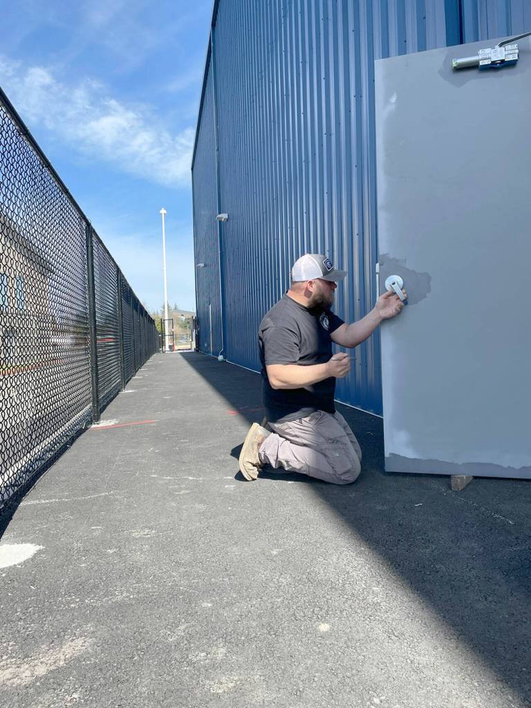 Ryan Rigby of ICI Construction paints doors on the lower level of the new Spartan Stadium in anticipation the ribbon cutting on April 14. The $2.5 million complex had been scheduled to open in October, but supply chain problems, poor weather and materials delivery delayed construction. (Paula Hunt/Peninsula Daily News)