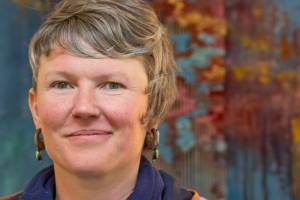 Artist Emily Carlquist, seen here before one of her abstract multi-media pieces featuring acrylic paint on textured canvas with needle-woven local fiber warped on canvas, on display at Dandelion Botanical for the month of April. (Emily Matthiessen/Olympic Peninsula News Group)