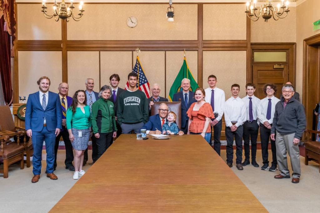 Gov. Jay Inslee, center, signs Substitute Senate Bill No. 5687 on April 25  legislation called the Charles Cate II Act that bolsters the creation and support of postsecondary wrestling grant programs. Joining Inslee are Cates son Charley and wife Renee. Behind Inslee is primary bill sponsor Sen. Kevin Van De Wege and Sequim wrestling advocate Randall Tomaras, along with wresters and wrestling advocates. At far right is SHS wrestling coach Steve Chinn. (Randy Tomaras/Gov. Jay Inslees office)