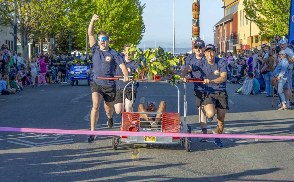 A team from East Jefferson Fire and Rescue jubilantly crosses the finish after overpowering the team from Arrow Lumber and Hardware to go undefeated in the round-robin event and win the Bed Races during the 2023 Rhody Festival on Saturday in downtown Port Townsend. Each bed must have some semblance of a bed with a headboard and footboard and wheels. Four pushers and a rider weighing at least 100 pounds or more are also required. (Steve Mullensky/for Peninsula Daily News)