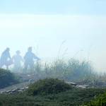 Firefighters receive assistance with a bucket of water from a Four Seasons Ranch resident while fighting a beach fire that threatened homes along the Strait of Juan de Fuca on Saturday. (Keith Thorpe/Peninsula Daily News)