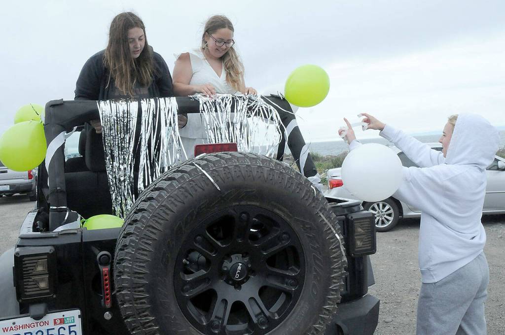 Port Angeles High School graduates Alyssa McCallister, left, and Cheyenne Zimmer get assistance from friend Ava Sheahan with decorating their ride prior to the start of Fridays Graduation Parade. About 100 vehicles with graduates, family and friends took part in the procession from Ediz Hook to Port Angeles High School. (Keith Thorpe/Peninsula Daily News)