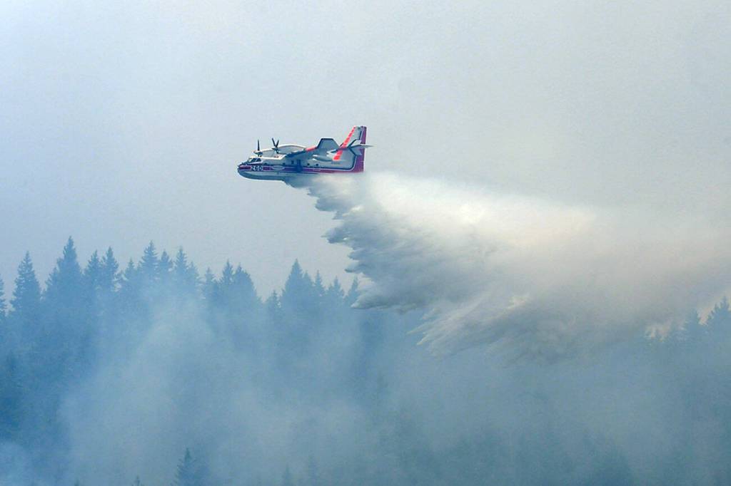 A Super Scooper aircraft makes a water dump on a flaming area of forest on Sunday in the Indian Creek Valley southwest of Port Angeles. (Keith Thorpe/Peninsula Daily News)