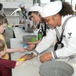 Banji Mullins, 3, left front, and Zachy Mullins, 6, both of Port Angeles, get temporary tattoos from USS Monsen crew members STG3 Anthony Mattioli of Cave Creek, Ariz., and STG3 Kortney Burnside of Hanford, Calif., at the Kids Zone activity fair at The Gateway in Port Angeles on Tuesday. (Keith Thorpe/Peninsula Daily News)