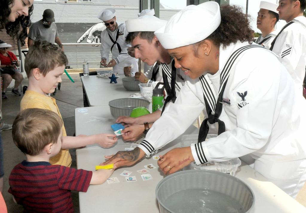 Banji Mullins, 3, left front, and Zachy Mullins, 6, both of Port Angeles, get temporary tattoos from USS Monsen crew members STG3 Anthony Mattioli of Cave Creek, Ariz., and STG3 Kortney Burnside of Hanford, Calif., at the Kids Zone activity fair at The Gateway in Port Angeles on Tuesday. (Keith Thorpe/Peninsula Daily News)
