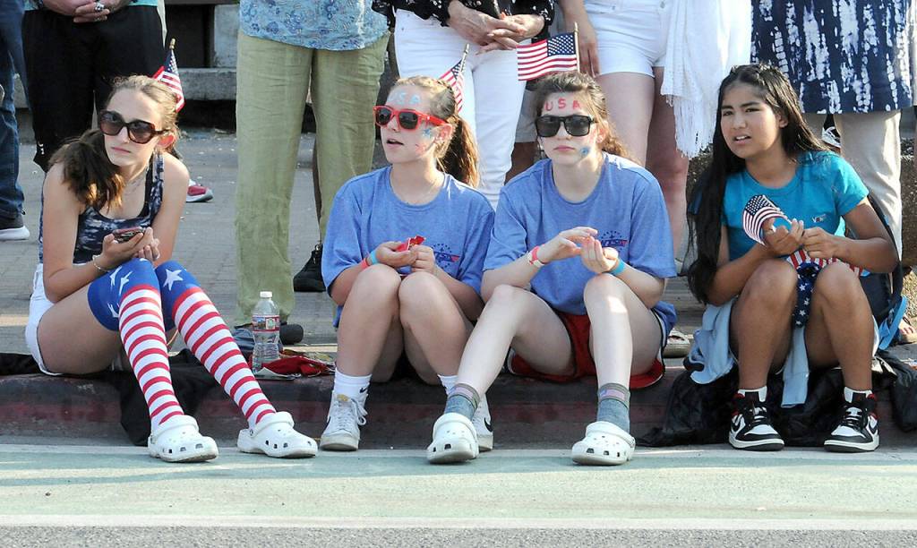 Port Angeles parade-goers, from left, Cate Chance, 13, Addy Fox, 13, Miriam Cobb, 13, and Angela Valles, 11, watch the festivities from a curb at First and Laurel streets on Independence Day in Port Angeles. (Keith Thorpe/Peninsula Daily News)