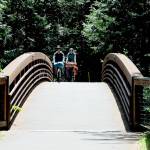 Tom Rooney of Seattle, left, and Marie Cazanave of Montreal, Quebec ride their bicycles over a 201-foot long footbridge spanning a small creek on Thursday at Sequim Bay State Park east of Sequim. (KEITH THORPE/PENINSULA DAILY NEWS)