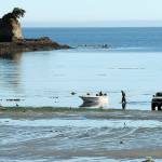 Greg Holmquist of Port Angeles walks to his beached boat to pull it to a waiting trailer, parked more than 100 yards from the end of the regular boat ramp as a group of kayakers paddle around the Bachelor Rock sea stack during Thursdays minus-2 low tide at Freshwater Bay west of Port Angeles. Holmquist said it was a perfect day for boating with calm seas and pleasant weather. (Keith Thorpe/Peninsula Daily News)