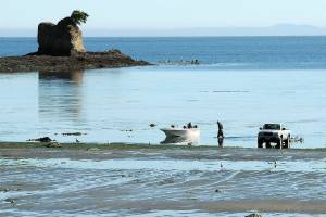 Greg Holmquist of Port Angeles walks to his beached boat to pull it to a waiting trailer, parked more than 100 yards from the end of the regular boat ramp as a group of kayakers paddle around the Bachelor Rock sea stack during Thursdays minus-2 low tide at Freshwater Bay west of Port Angeles. Holmquist said it was a perfect day for boating with calm seas and pleasant weather. (Keith Thorpe/Peninsula Daily News)