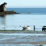 Greg Holmquist of Port Angeles walks to his beached boat to pull it to a waiting trailer, parked more than 100 yards from the end of the regular boat ramp as a group of kayakers paddle around the Bachelor Rock sea stack during Thursdays minus-2 low tide at Freshwater Bay west of Port Angeles. Holmquist said it was a perfect day for boating with calm seas and pleasant weather. (Keith Thorpe/Peninsula Daily News)