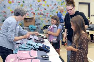 Julia Smith of Port Angeles, center right, oversees her children, fourth-grader Julia Smith, 9, and fifth-grader Shelby Smith, 10, right, pick out backpacks filled with school supplies as volunteer Ann West assists with distribution during Saturdays back-to-school fair at Jefferson Elementary School in Port Angeles. During the event, students were given free school supplies, with family service opportunities, as well as a lunch, made available at the approach of the 2023-24 school year. (Keith Thorpe/Peninsula Daily News)