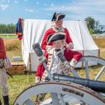 Dressed as British soldiers at the time of the American Revolution, Peter Berneking of Sequim, Thomas House-Higgins of Olympia and Luke Berneking explain about how a three pound ball fits into this particular cannon while Caleb Berneking looks on during the 2022 event.