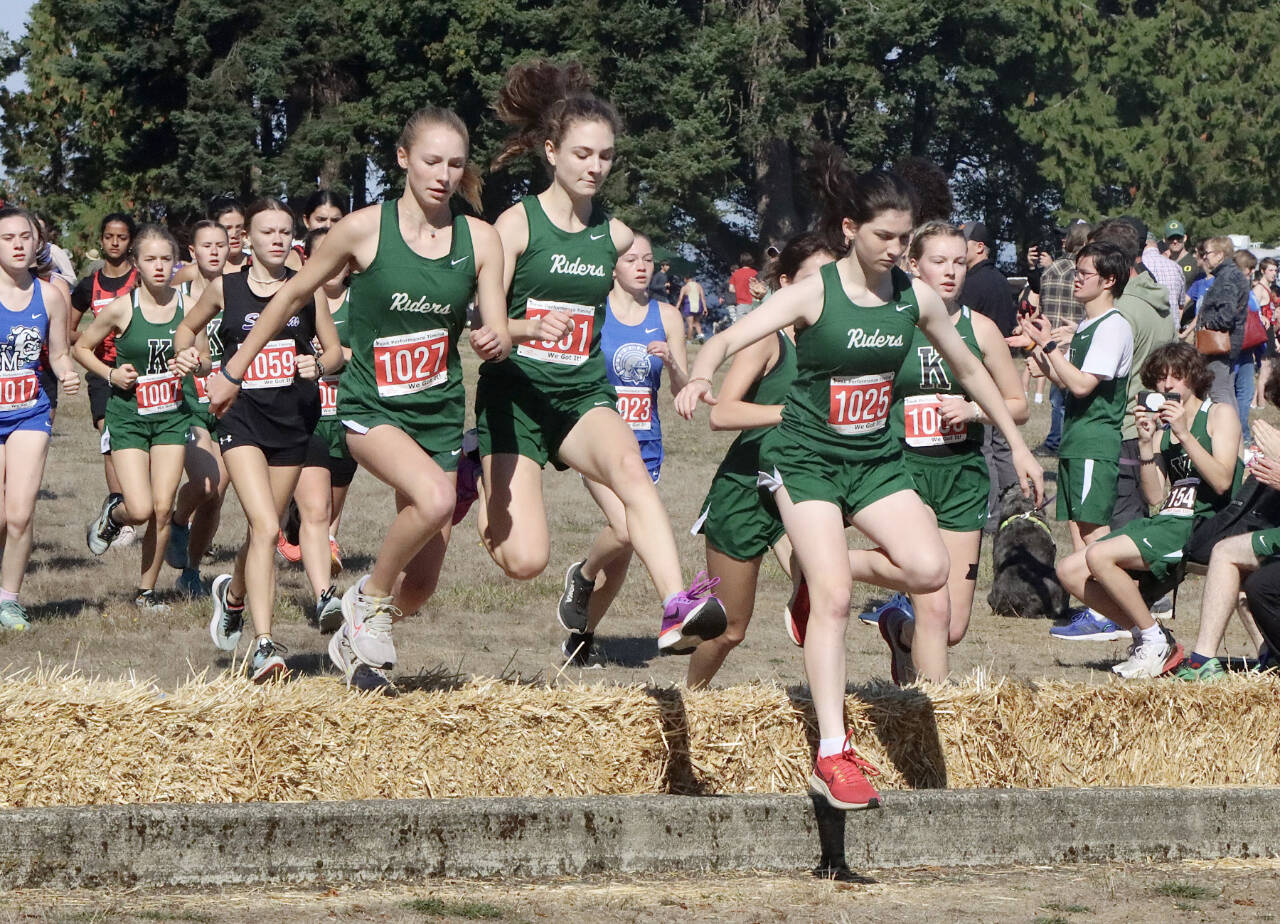 Port Angeles Leia Larson, Faerin Tate and Miriam Cobb jump over the hay bales at the start of the 45th annual Salt Creek Invitational at Salt Creek County Park on Saturday. Larson and Cobb both finished in the to 10 while all three Roughriders finished in the top 20. (Dave Logan/for Peninsula Daily News)