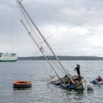 Unidentified men work to try to pull the partially sunken, 36-foot ketch Touchstone off the sand after it was blown off its anchorage during a windstorm that blew across Port Townsend Bay on Friday night and Saturday morning. Another round of gusty winds is expected today. (Steve Mullensky/for Peninsula Daily News)