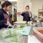 Salish Sea Ecotourism and Hospitality student Julia Livingston, 17, left, dices basil while Trinity Williams, 18, creates garlic bread twists at the Port Angeles School Districts commercial kitchen classroom. (KEITH THORPE/PENINSULA DAILY NEWS)<address><em></em></address>