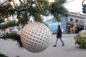 A Christmas ornament hangs from the downtown Port Angeles Christmas tree as a pedestrian walks past the plaza at the Conrad Dyar Memorial Fountain. The tree, towering above the intersection at First and Laurel streets, will remain illuminated through the holiday season. (Keith Thorpe/Peninsula Daily News)