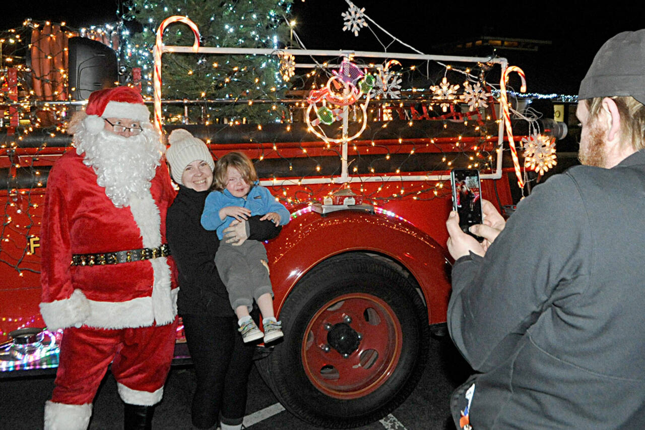 Veronica Weatherly holds her son Tucker for a photo-op with Santa Claus in 2021 as her husband Doug takes a photo. Santas Toy and Food Fire Brigade tours Sequim again Dec. 4-7. (Matthew Nash/Olympic Peninsula News Group)