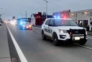 DAVE LOGAN/FOR PENINSULA DAILY NEWS A parade honoring Ron Cameron, with nearly two dozen vehicles with lights flashing, heads east on First Street in Port Angeles.