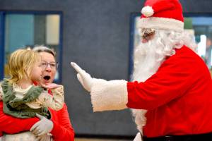 Santa Claus, portrayed by Stephen Rosales, greets Paisley Schroeder, 2, and Deb Bemm at a Christmas lunch in Sequim on Monday at the Carroll C. Kendall Unit of the Boys and Girls Clubs of the Olympic Peninsula. The annual lunch is hosted by the Khela family of Sequim which began hosting a community meal on Christmas 10 years ago as a way of giving back to the community. This year 20 turkeys and 10 hams were cooked to feed whats estimated to be about 400 people. Children were able to choose up to four gifts, donated to the event by community members and the local branch of Toys for Tots. (Peter Segall/Peninsula Daily News)