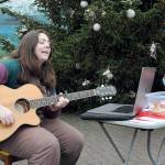 Kenzie Carney of Port Angeles plays guitar and sings while giving away candy canes, oranges and homemade cookies in front of the downtown Port Angeles Christmas tree at the Conrad Dyar Memorial Fountain on Tuesday. (KEITH THORPE/PENINSULA DAILY NEWS)