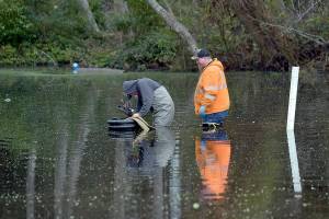 Michael Poats, left, and Brody Merritt of the Port Angeles stormwater department work to install a pump to remove standing water from a flooded area near the playground at Shane Park in Port Angeles on Wednesday. The pool of standing water, which is up to 3 feet deep in places and has at times covered the nearby play equipment, is to be pumped to a nearby storm drain. (Keith Thorpe/Peninsula Daily News)